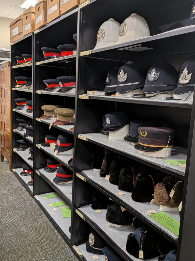Shelves filled with Calgary Police uniform hats, including vintage helmets, peaked caps, and fur hats, all neatly organized and labeled as part of a historical collection.