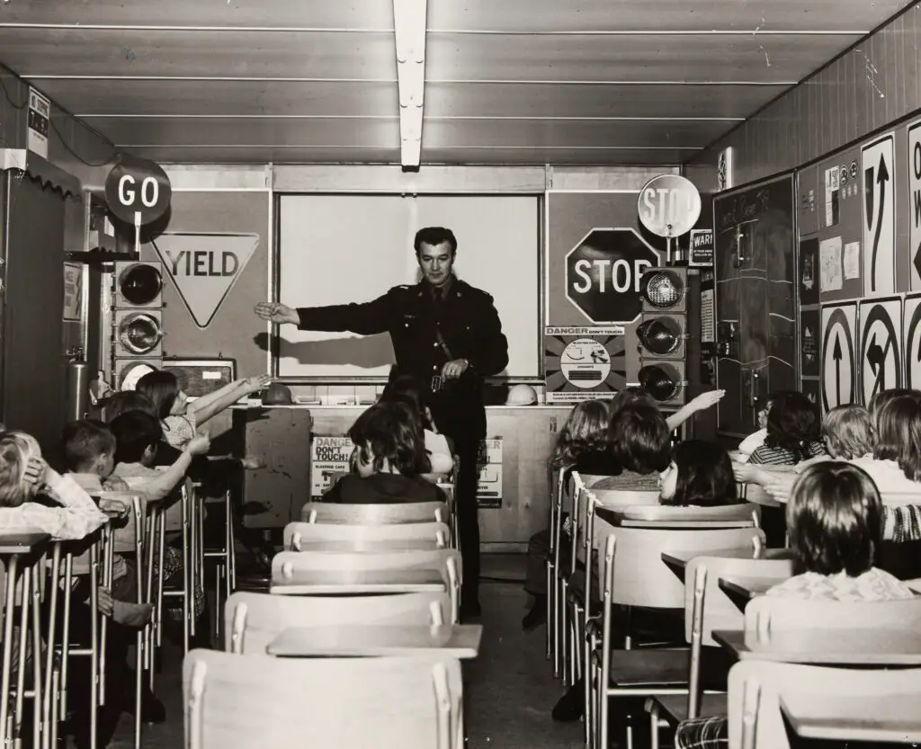 Calgary Police officer teaching children about traffic safety in a classroom decorated with stop signs, yield signs, and a working traffic light.